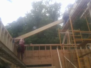 Carpenter raising a rafter beam on a new second story frame in White Hall