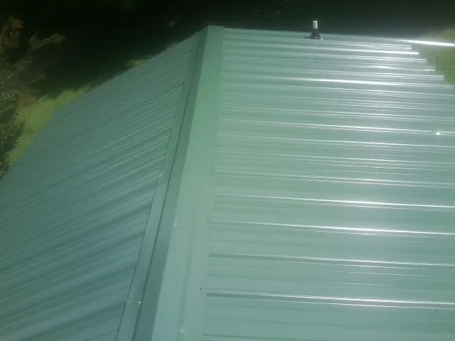 New green metal panels meeting at the ridge of a roof — Flat Roof Repair work by our crew in White Hall