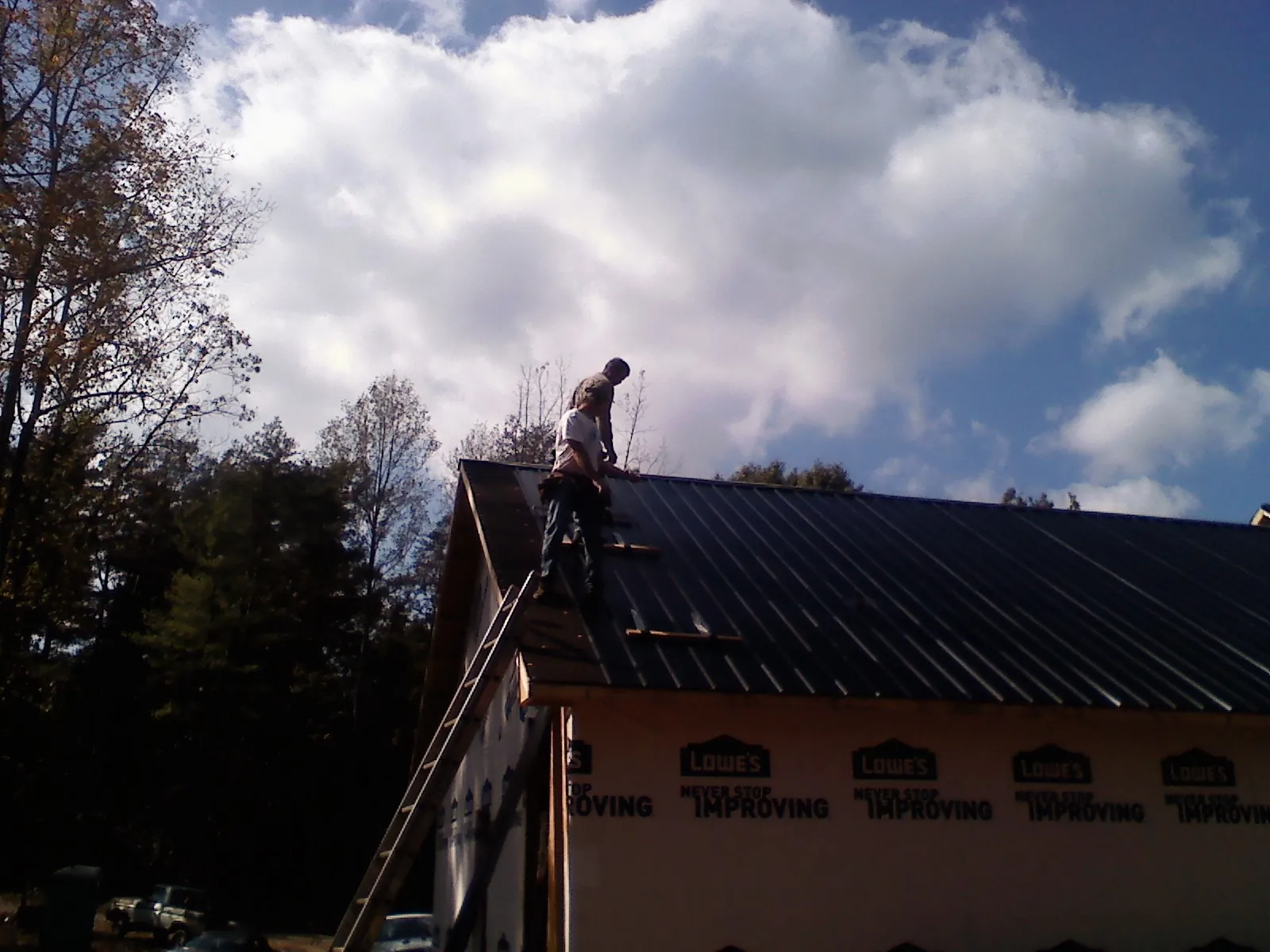Roofer fastening dark metal panels high against a cloudy sky, from a Roof Inspection job in White Hall